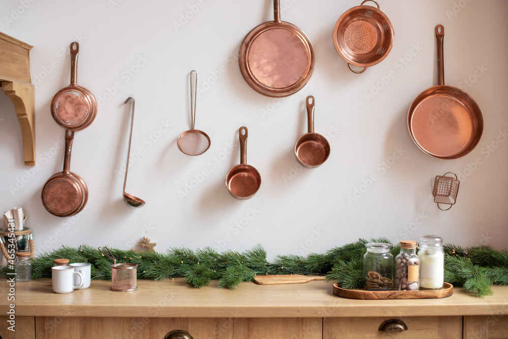Set of saucepans hanging in kitchen. Hanging Copper kitchen utensil on the white wall. Different kind of vintage copper cookware, pans, pots and funnel on wooden kitchen. Rustic kitchen interior decor - obrazy, fototapety, plakaty 