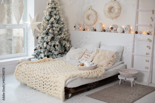  Interior design bedroom. New year winter home interior decor. White bedroom with christmas tree and comfortable bed and pillows, copy space. concept new year and holidays. Scandinavian room style.