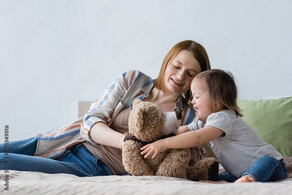 Smiling woman playing with daughter with down syndrome and soft toy on bed. Smiling woman playing with daughter with down syndrome and soft toy on bed.
