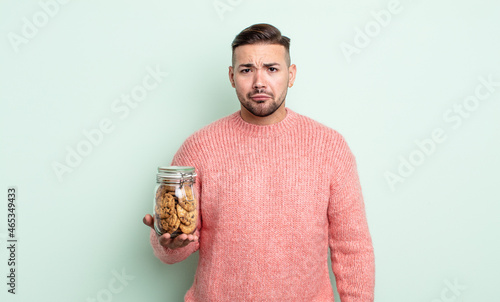 young handsome man feeling sad and whiney with an unhappy look and crying. cookies bottle concept photo