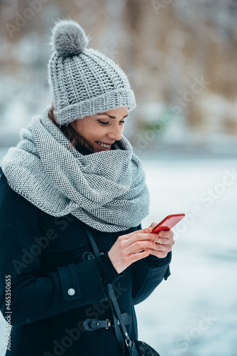 Beautiful young woman using smartphone and wearing scarf and a a hat on a cold winter day © Zamrznuti tonovi