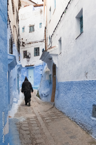 In the medina of Chefchaouen in Morocco. A man dressed in the traditional Berber coat walks down an alley lined with blue walls © Louis-Michel DESERT