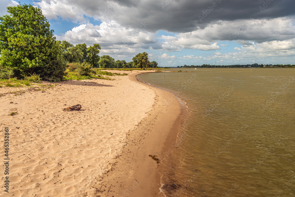 Sandy beach of the Dutch river Waal near Slot Loevestein near the village of Poederoijen in the province of Gelderland. It is a sunny and cloudy day at the end of the summer season.