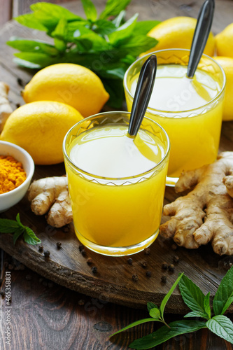 Immune booster antivirus drink, turmeric with ginger, lemon, mint and spices hot winter tea on wooden rustic background, closeup, natural medicine and naturopathy concept