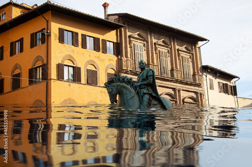 Mediterranean square with village houses and statue in floodwater. Road with overflown water. Floods and flooding the streets. Natural disaster. Manipulated image.