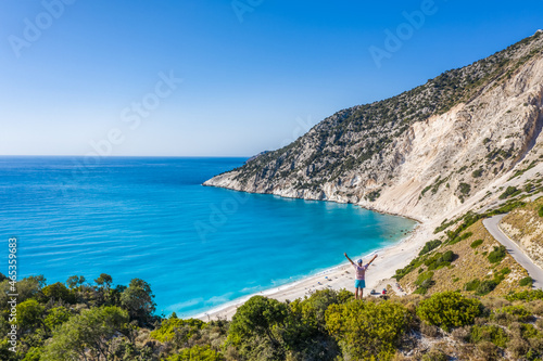 Man tourist standing on top of a rock, raising hands with an exciting feeling of freedom, looking at Myrtos Beach. Cephalonia island, Greece © Igor Tichonow