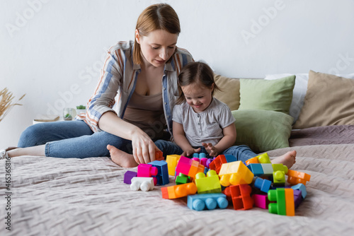 Woman and child with down syndrome playing building blocks on bed at home.