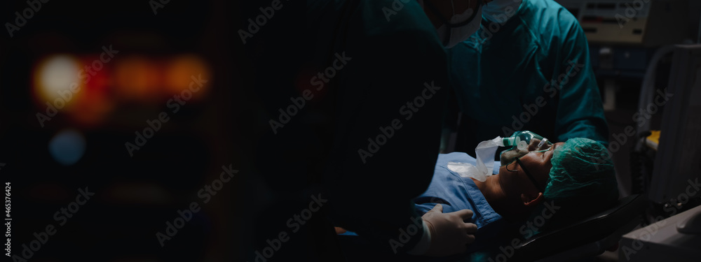 Patient wear a medical ventilator lying on the surgical bed in the operating room with surgeon stand by his side to keep an eye on the symptoms at hospital in night time in banner with copy space