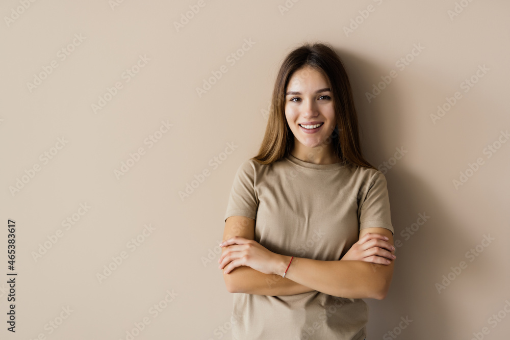 Charming woman standing with hands folded, looking at camera, isolated over beige background Charming woman standing with hands folded, looking at camera, isolated over beige background