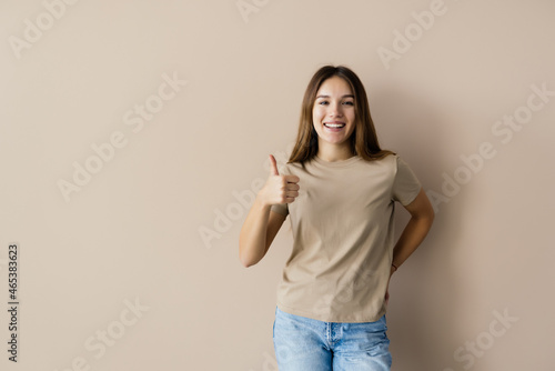 Cheerful blonde woman showing thumb up at camera isolated over beige background