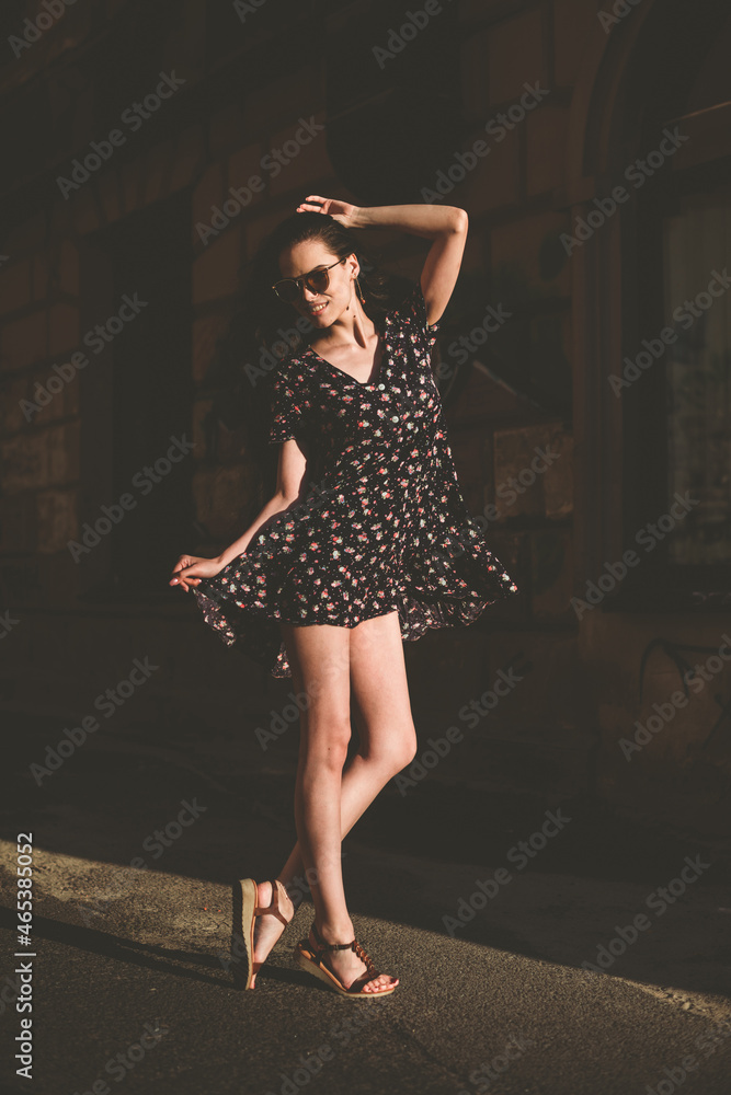 Portrait of stylish young woman. Brunette with curly hair in sundress posing on street. selective focus Portrait of stylish young woman. Brunette with curly hair in sundress posing on street. selective focus