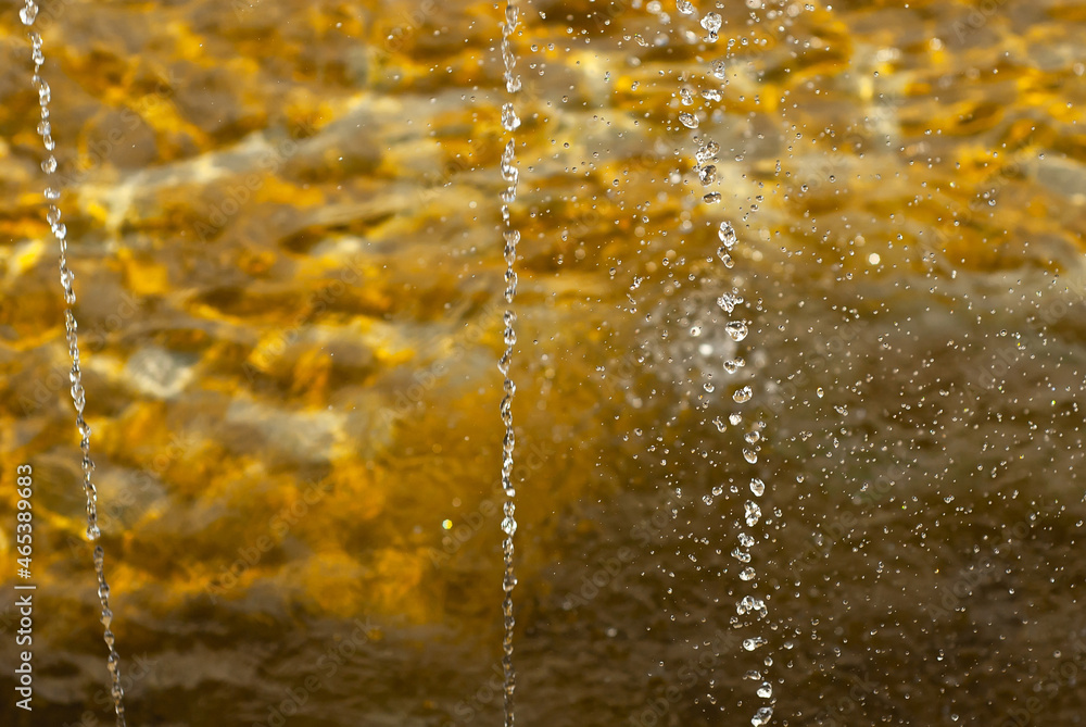 Water drops from a fountain close up. Jet fountain on a sunny day. Sharpness on the front drops of water. Water drops from a fountain close up. Jet fountain on a sunny day. Sharpness on the front drops of water.
