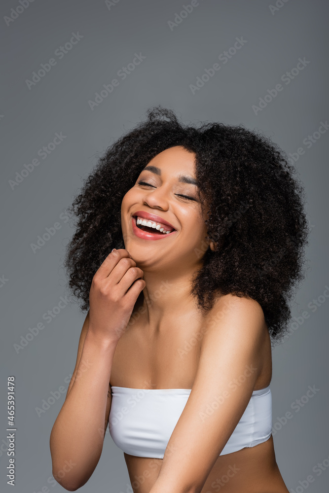 excited african american woman in white top laughing with closed eyes isolated on grey excited african american woman in white top laughing with closed eyes isolated on grey