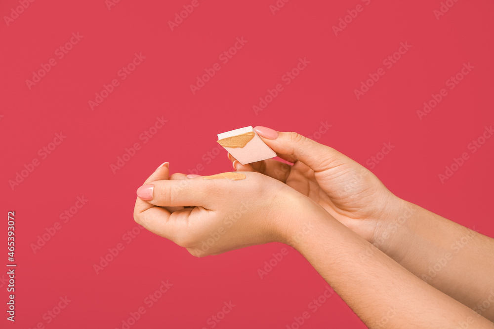 Woman putting foundation with makeup sponge on her wrist on color background Woman putting foundation with makeup sponge on her wrist on color background