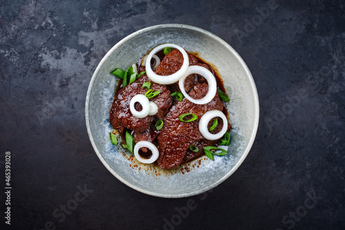 Modern style traditional Cuban dry aged angus bistec encebollado steak with onion rings in soy sauce served as top view in a Nordic design bowl with copy space photo