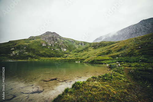 Atmospheric mountain landscape with rainy circles on clear lake water. Sandy bottom of mountain lake with stones. Beautiful scenery with circles of rain on transparent water surface in rainy weather.