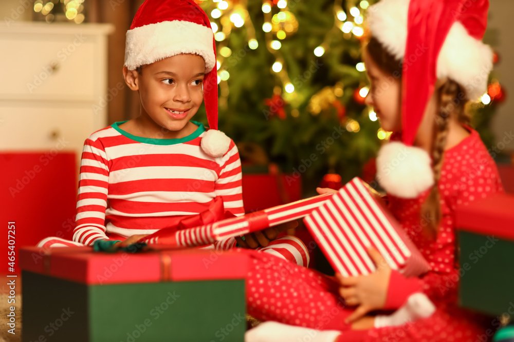 Little children in Santa hats with Christmas gifts at home