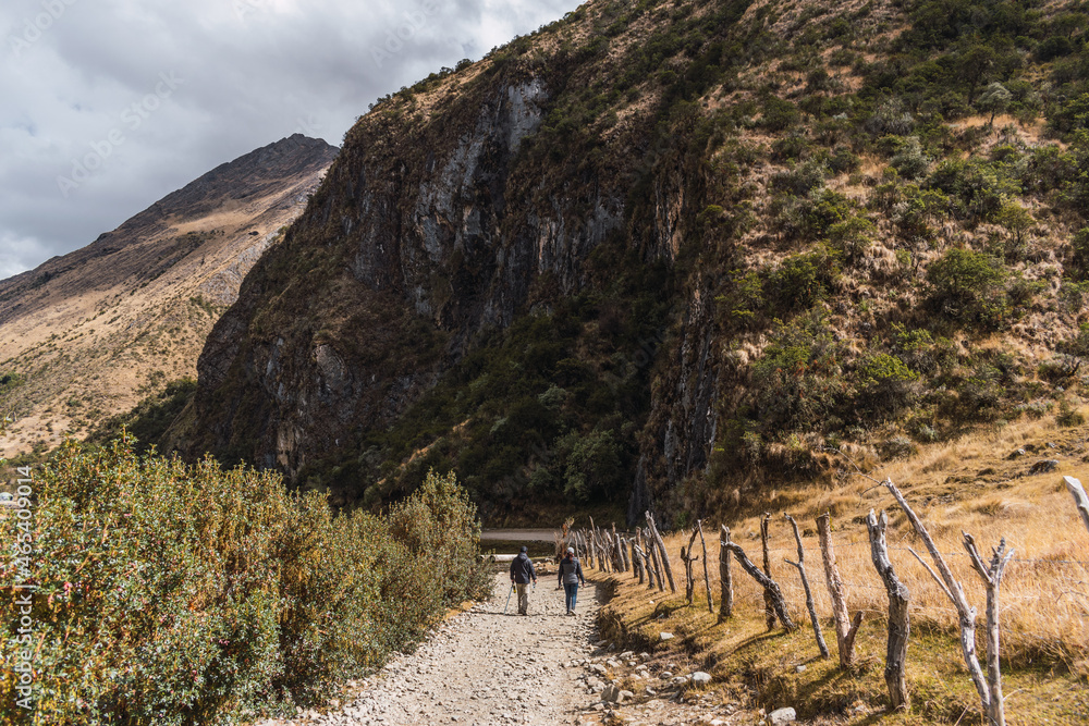 couple walking on a path surrounded by mountains and green vegetation on a sunny day with clouds and blue sky in the Andes of Peru