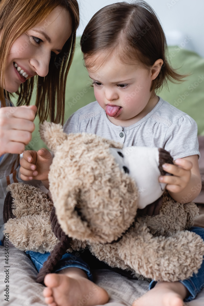 Smiling woman playing with baby daughter with down syndrome and soft toy on bed. Smiling woman playing with baby daughter with down syndrome and soft toy on bed.