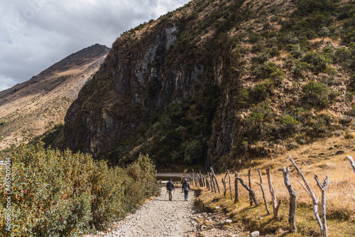 Fototapeta Naklejka Na Ścianę i Meble -  couple walking on a path surrounded by mountains and green vegetation on a sunny day with clouds and blue sky in the Andes of Peru