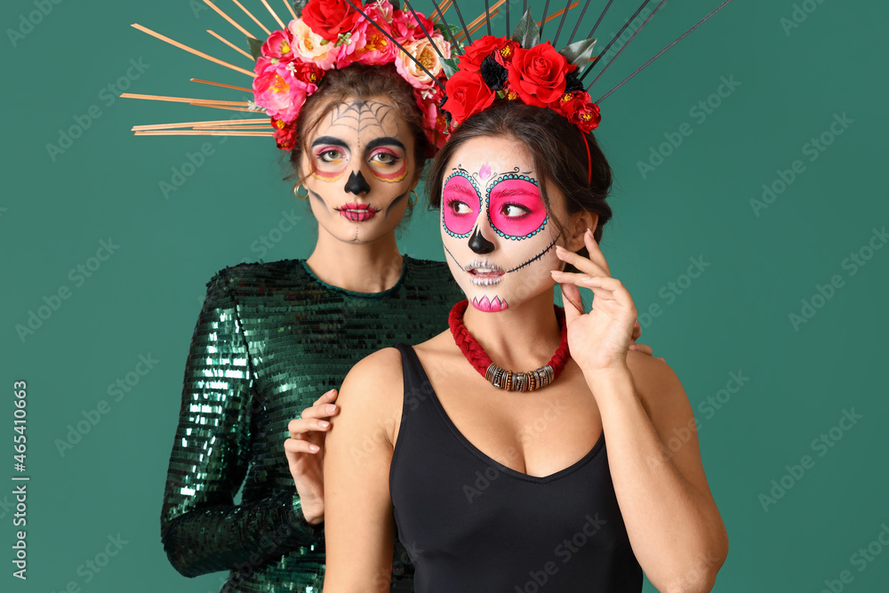 Fototapeta premium Stylish women with painted skull on faces against color background. Celebration of Mexico's Day of the Dead (El Dia de Muertos)