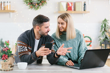 Young couple husband and wife working together online at home, with laptop sitting in the kitchen, happy together, during the New Year and Christmas holidays