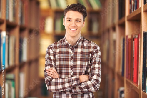 Smiling businessman stands and looks at the camera. Young positive male student in library