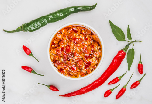 Chili hot peppers oil sauce seasoning and fresh chili peppers red and green on white marble background copy space.