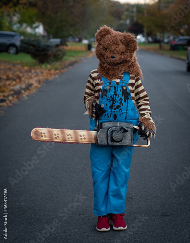 Child with scary Halloween costume of bear mask and chainsaw