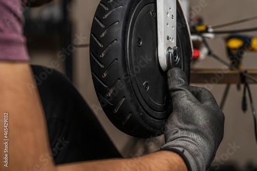 Close up of an unrecognizable mechanic adjusting the electric scooter wheel with a wrench