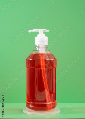 Plastic bottle of liquid red soap on green background