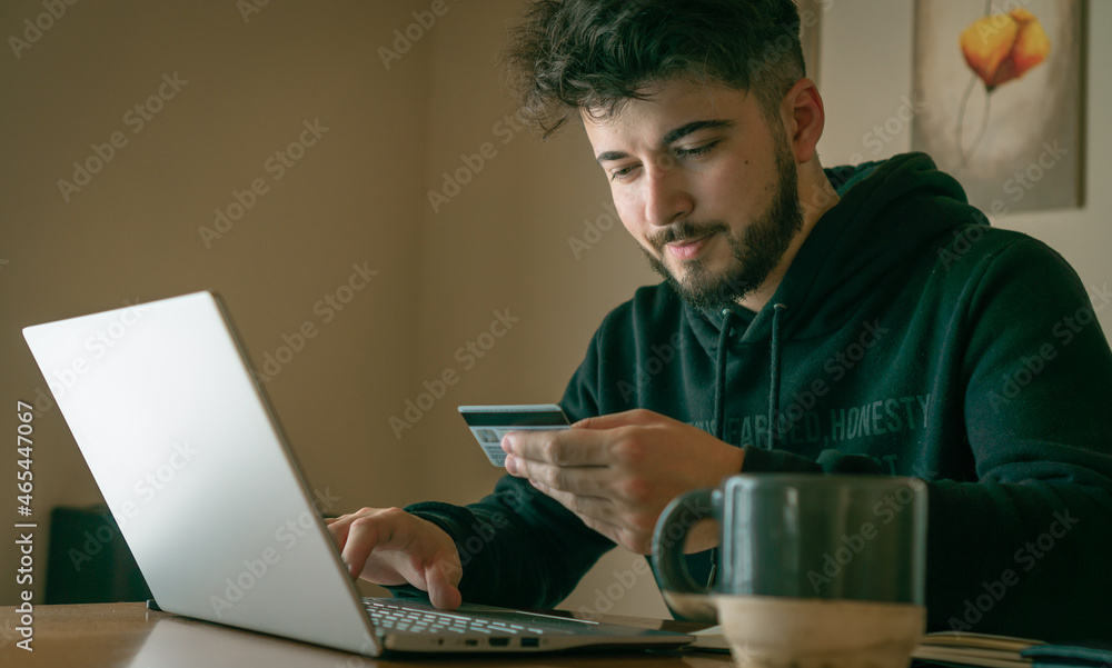 young man making online purchases with a card in front of a laptop young man making online purchases with a card in front of a laptop