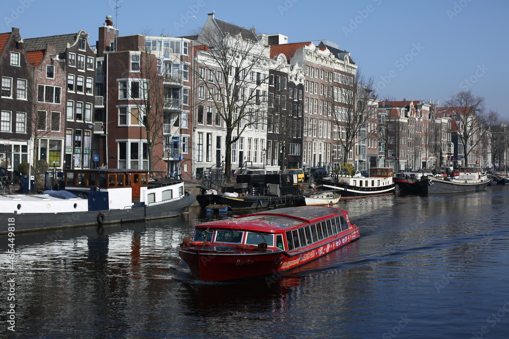 scenery of traditional brick houses and a red long tour boat sailing in canal in winter amsterdam