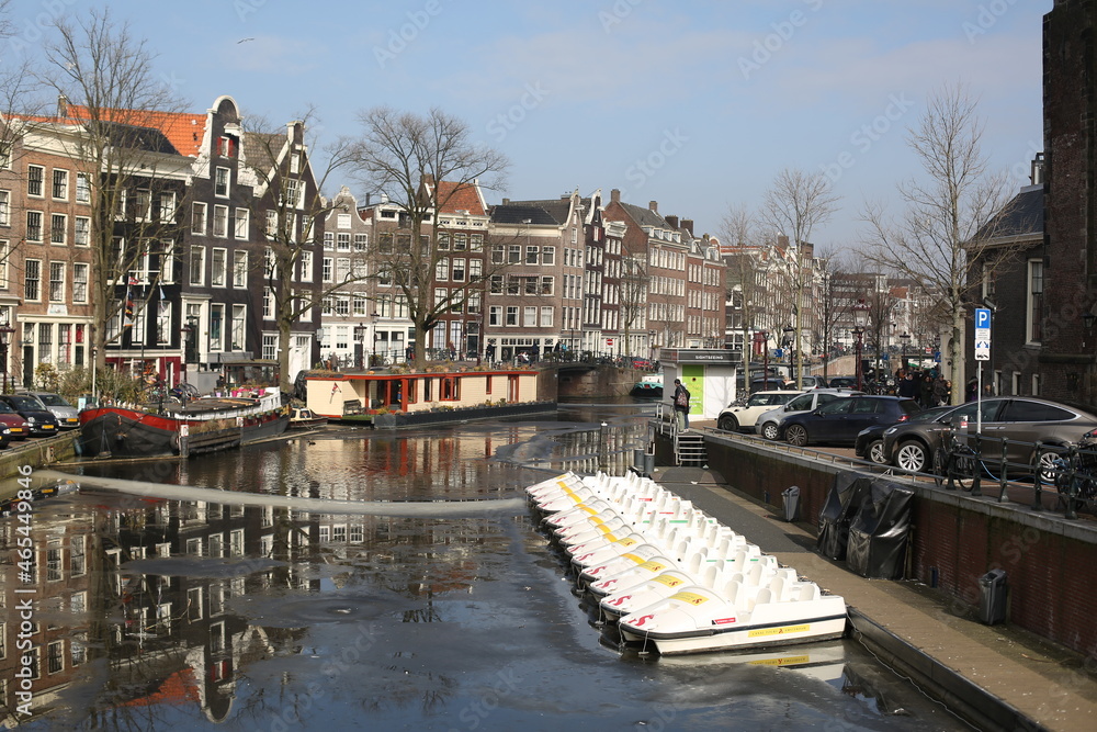 the scenery of traditional brick houses and white small boats moored at the shore of the canal of winter Amsterdam