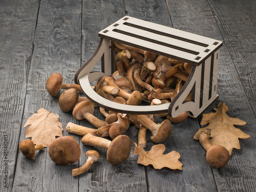 An inverted wooden box with autumn mushrooms and leaves on a wooden table.