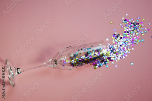 Fototapeta Naklejka Na Ścianę i Meble -  The champagne glass is filled with shiny stars that are scattered on a pink background. A party with a festive mood.  Christmas, the concept of celebration.