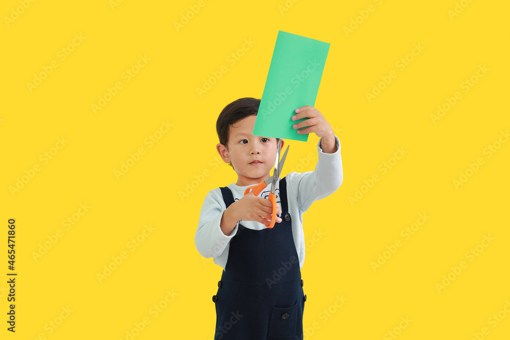 Asian little boy enjoys craft work by scissors cut the color paper isolated on yellow background. Image with Clipping path. Asian little boy enjoys craft work by scissors cut the color paper isolated on yellow background. Image with Clipping path.