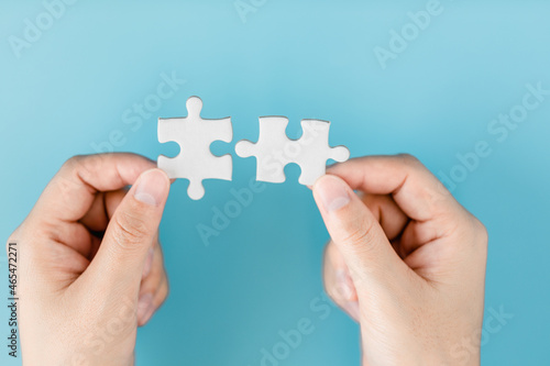 Close up of hand women connecting pieces of a jigsaw puzzle on a blue background, business connection, success, solution, and strategy concept.