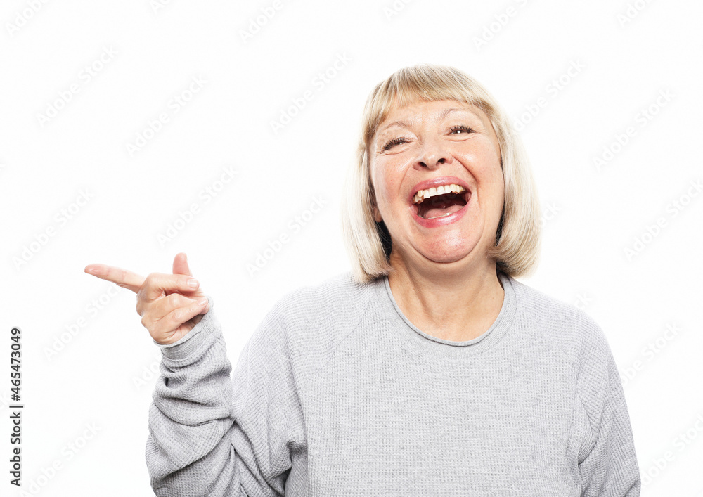 Smiling elderly blonde woman lady 60s years old in casual sweater pointing index finger aside up on mock up copy space Smiling elderly blonde woman lady 60s years old in casual sweater pointing index finger aside up on mock up copy space