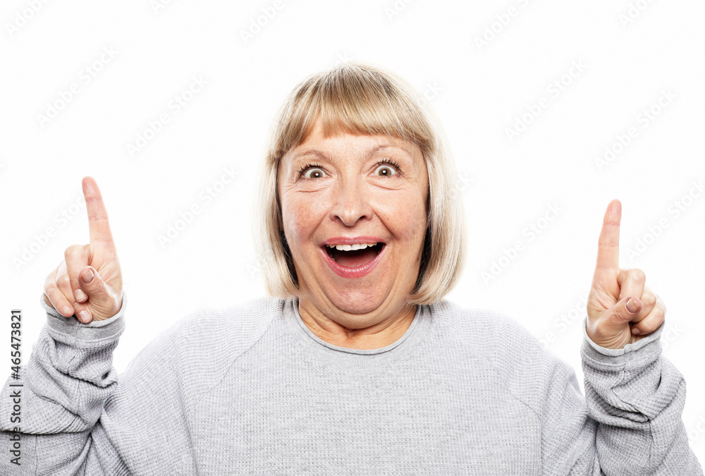 Beautiful elderly female model with optimistic expression indicates upwards, being excited by something, raises fore finger Beautiful elderly female model with optimistic expression indicates upwards, being excited by something, raises fore finger