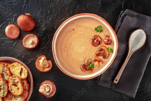 Mushroom cream soup with various mushrooms and toasted bread, overhead flat lay shot on a black slate background