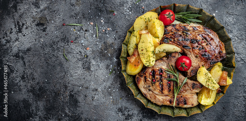 Grilled pork steak with potatoes and vegetables. Long banner format. top view