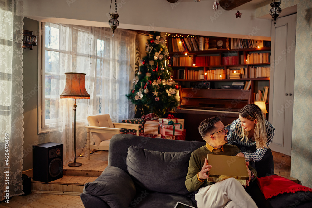 Young woman surprising her boyfriend with a Christmas gift at home Young woman surprising her boyfriend with a Christmas gift at home