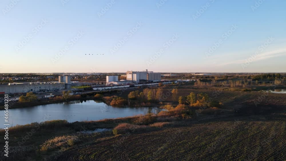 aerial view of harvested farm field in rural eastern Wisconsin with retention pond, urban city, and train logistical station in background aerial view of harvested farm field in rural eastern Wisconsin with retention pond, urban city, and train logistical station in background