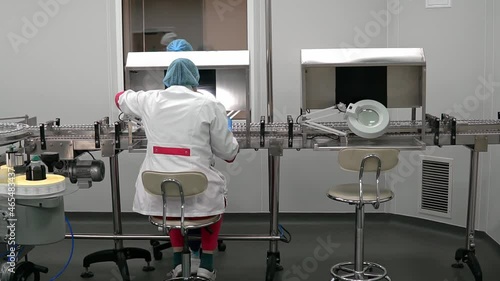 Pharmacologist worker makes quality control of medical products. Empty glass bottles on automatic production line machine conveyor. Vaccine Mass Production in Laboratory. ampoules with medicine