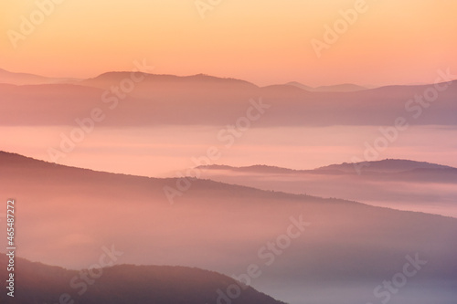 autumnal rural landscape. beautiful nature scenery with foggy valley and glowing sky at sunrise. trees in colorful foliage and fields on hills in morning light