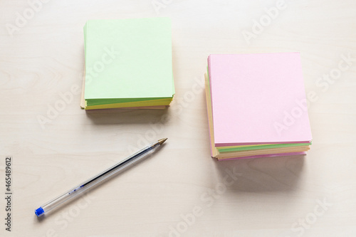 top view of stacks of blank colorful sheets of memo paper and simple blue pen on light brown wooden board