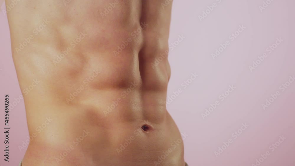 Male bodybuilder poses in studio demonstrating results of training in gym and fitness classes, closeup abs, pink background, front view. Man of athletic build shows body Male bodybuilder poses in studio demonstrating results of training in gym and fitness classes, closeup abs, pink background, front view. Man of athletic build shows body