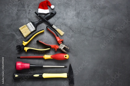 Creative Christmas tree made of construction tools on a gray background with santa claus hat. Industrial greeting card and happy new year creative concept.