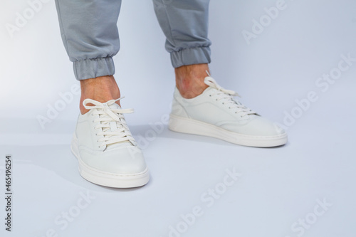 Men's feet in white everyday sneakers made of natural leather on lacing.